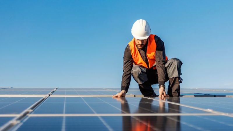 Symbolfoto eines Handwerkers bei der Installation von Solarzellen auf einem Dach.