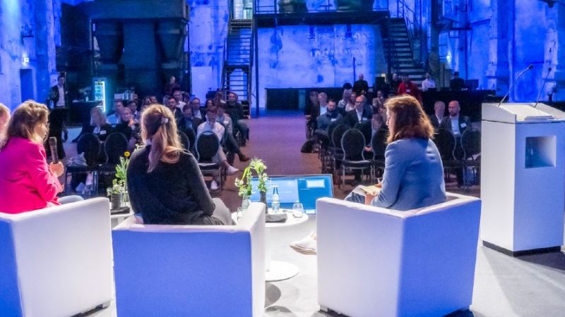 Podium von hinten fotografiert auf die sitzenden Teilnehmenden schauend