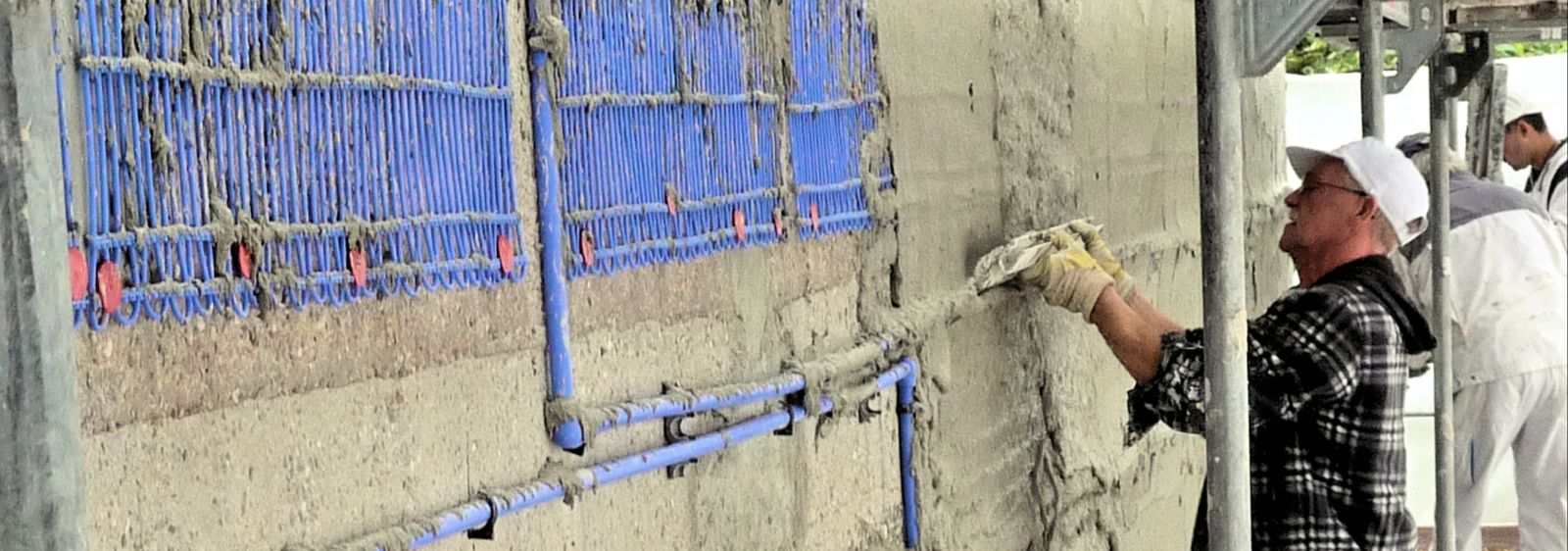 The capillary tube mats are applied to the outside of the facade as a surface heating system. In the picture, the adhesive mortar is being smoothed for the light plaster.