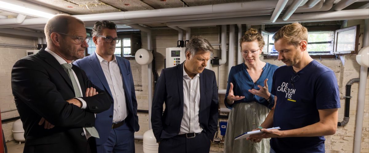 Dr Arwen Colell, Managing Director of decarbon1ze, Jan Weil, Co-CTO, use the pilot installation in a Vonovia boiler room to explain how small-scale flexibilities can also relieve the energy system behind the meter. from left to right: Stefan Kapferer, CEO 50Hertz, Stefan Ritter, Head of Energy at Vonovia, Federal Minister for Economic Affairs and Climate Action Robert Habeck, Dr Arwen Colell and Jan Weil, both decarbon1ze.