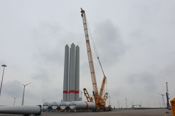 Vier Türme von Windenergieanlagen stehen nebenienander im Hafen, daneben ein gelber Kran.